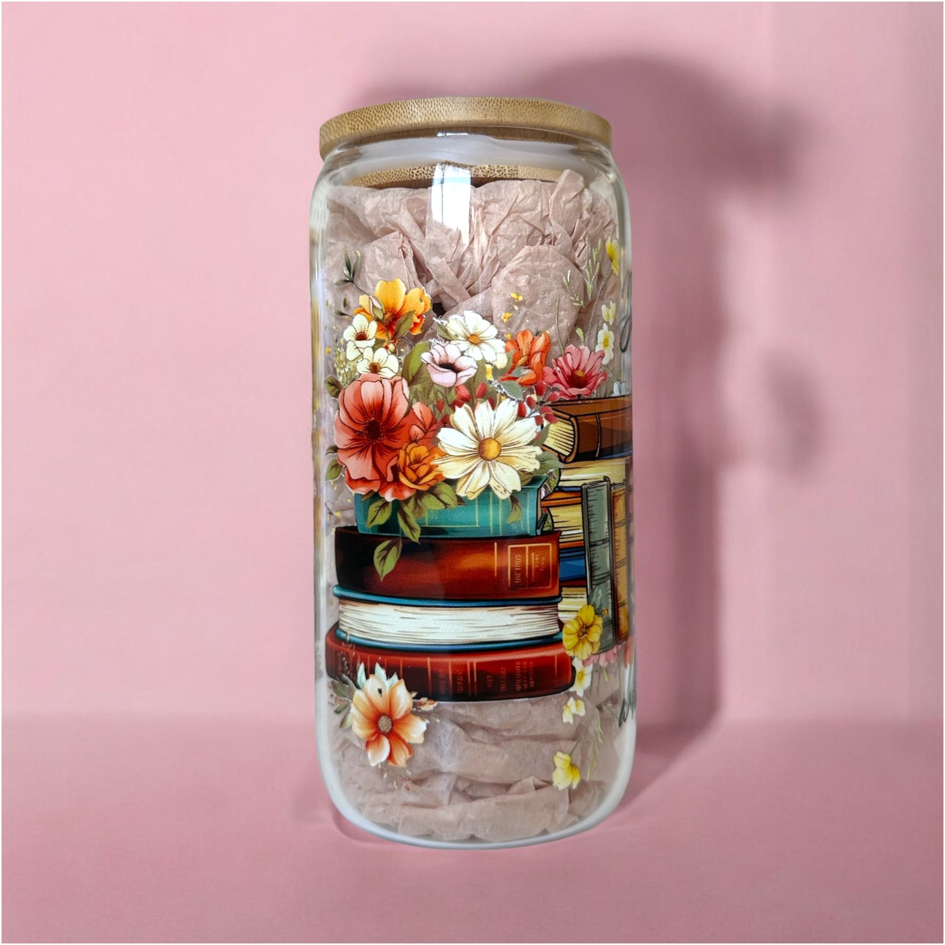 Glass cup with floral design and stacked books, perfect for book lovers and iced coffee enthusiasts.